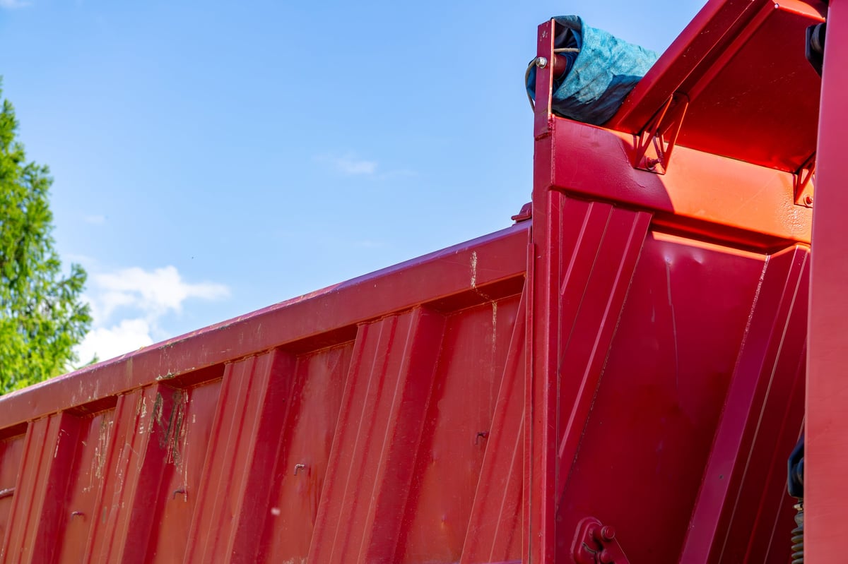 Red dump truck with open tailgate against blue sky