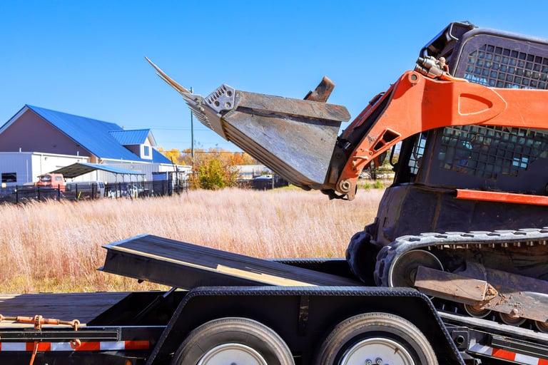 An excavator is unloading materials from flatbed trailer at construction site